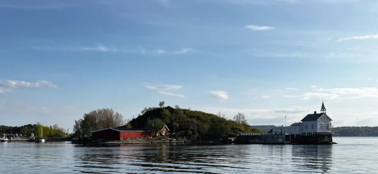 Im Vordergrund Wasser mit einem Gebäude und Hügel. Oslo Städtetrip