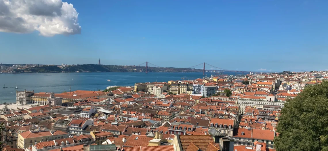 Lissabon: Eine Stadt mit roten Dächern und eine Brücke die über das Wasser führt.