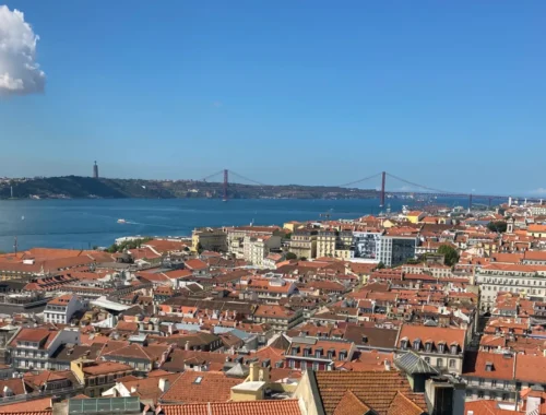 Lissabon: Eine Stadt mit roten Dächern und eine Brücke die über das Wasser führt.